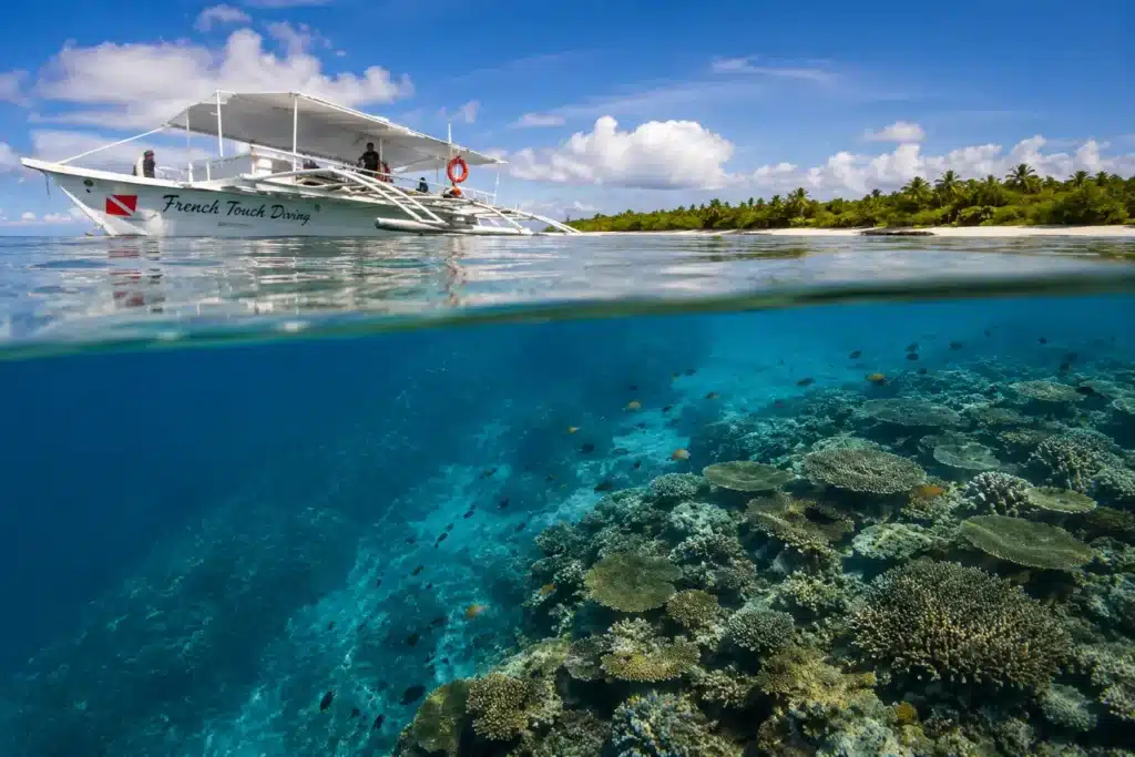 Bateau de plongée au-dessus des récifs coralliens de Pamilacan dans une mer calme et cristalline aux Philippines.
