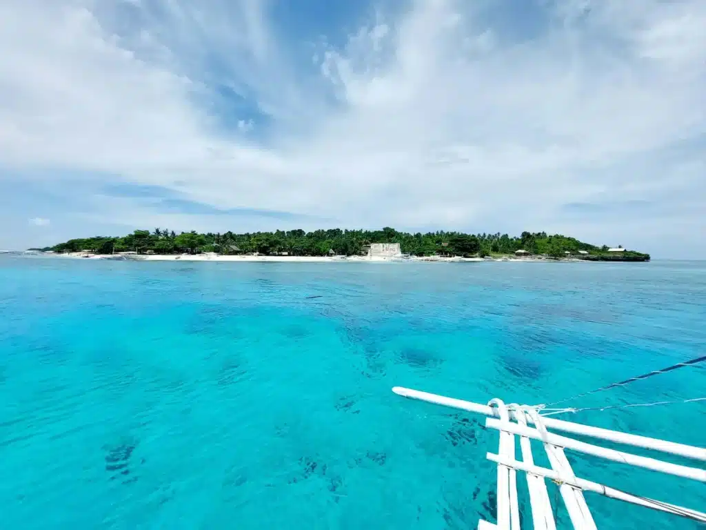 Vue sur l'île de Pamilacan depuis un bateau de plongée dans une eau turquoise cristalline aux Philippines.